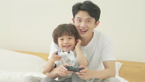 Happy-family-father,-child-son-playing-games-and-videos-on-bed-at-home-joyful-atmosphere-enjoying-leisure-time-in-living-room