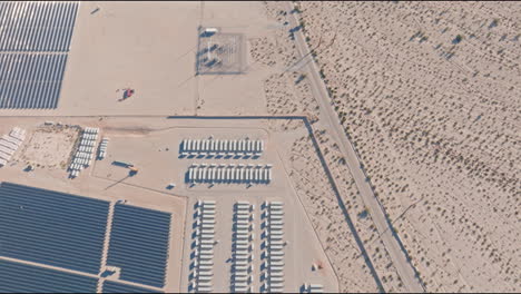 Drone-shot-over-solar-panels-and-storage-units-in-desert,-showcasing-expansive-layout-and-desert-terrain