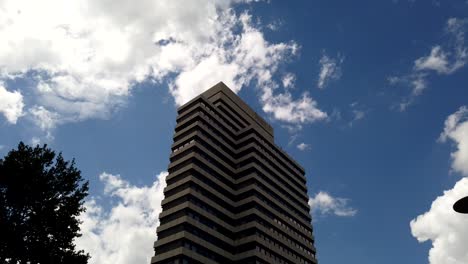 Time-lapse-Urbano,-Edificio-De-Oficinas-De-Gran-Altura-Contra-Nubes-Blancas-En-El-Cielo-Azul,-Vista-De-ángulo-Bajo