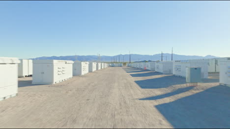 Drone-flying-through-rows-of-storage-units-at-desert-facility-surrounded-by-mountainous-landscape