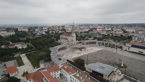 Plaza-De-Peregrinos-En-Fátima,-Portugal,-órbita-Aérea-Día-Nublado-Con-El-Horizonte-De-La-Ciudad