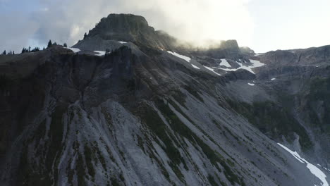 La-Hermosa-Luz-Del-Sol-Se-Difunde-Entre-Las-Nubes-En-La-Cima-De-La-Montaña-Con-Acantilados-Rocosos-Secos,-Ascenso-Aéreo