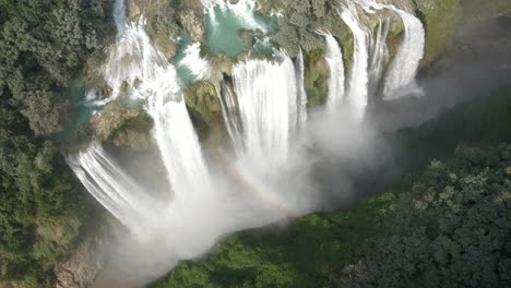 Drone-bird's-eye-view-of-Tamul-Waterfall-with-cascade-and-mist-creating-rainbow-light-arches