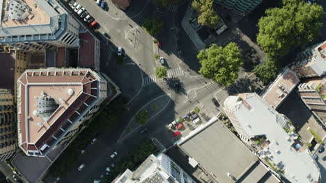 Drone-descends-on-intersection-half-in-shade-of-buildings-in-Trastevere-neighborhood-Rome-Italy-as-cars-drive-streets