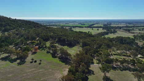 Aerial-pan-around-over-green-farmland-with-farmhouses-cattle-and-dams-near-Euroa