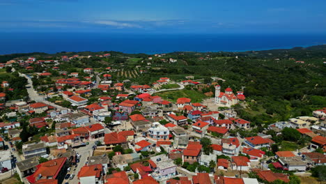 Un-Pueblo-Costero-Con-Casas-Con-Techos-Rojos-Rodeado-De-Exuberante-Vegetación-Y-Mar-Azul,-Vista-Aérea