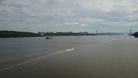 Drone-Sigue-A-Un-Barco-En-El-Río-Hudson---Ciudad-De-Nueva-York,-Fondo-Del-Puente-De-Lavado-De-Midtown-George