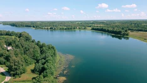 Luftaufnahmen-Zeigen-Einen-Ruhigen-See,-Umgeben-Von-üppigem-Grün-Und-Ländlichen-Häusern-Unter-Einem-Klaren-Blauen-Himmel