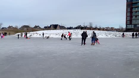 People-enjoy-ice-skating,-sledding-and-ice-walking-on-a-frozen-pond-in-a-city-park-during-the-freezing-cold-in-February,-which-lasted-only-one-week-in-the-Netherlands-in-2021