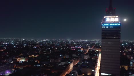 Aerial-Rising,-Latinoamericana-Tower-Skyscraper-Glowing-at-Night-in-Mexico-City