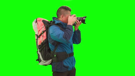 An-adult-tourist-with-backpack-stands-in-a-studio-with-green-screen,-holding-a-camera