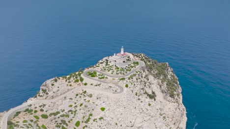 Flying-over-rugged-limestone-coastal-cliff-with-lighthouse-tower,-Mallorca