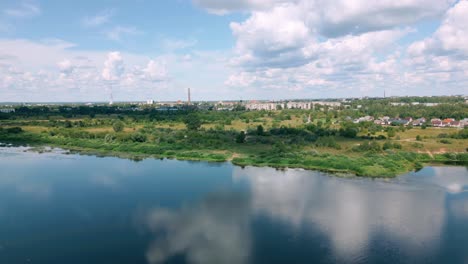 Aerial-footage-of-Daugavpils,-Latgola,-Latvia,-showcasing-the-Daugava-River-reflecting-the-sky,-with-the-city's-landscape-and-buildings-in-the-background