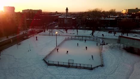 Toma-Aérea-Girando-Alrededor-De-Una-Pista-De-Hockey-Al-Aire-Libre-En-Montreal-Con-Jugadores-Al-Atardecer,-Creando-Una-Agradable-Luz-Brillante.