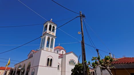 Slow-motion-landscape-of-church-bell-tower-architecture-historic-buildings-in-main-town-square-street-with-electricity-power-lines-Greece-Europe-travel-tourism