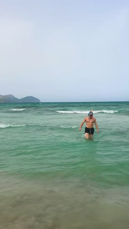 Vertical---muscular-caucasian-male-walk-out-of-turquoise-water,-Mallorca