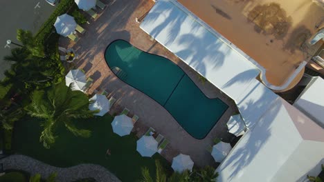 Aerial-view-rising-above-a-pool-at-the-Colony-hotel,-on-a-sunny-morning,-in-Palm-Beach,-Miami,-Florida,-USA---screwdriver,-drone-shot