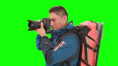 Adult-man-with-backpack,-posing-in-a-studio-with-green-screen,-takes-pictures-with-a-camera