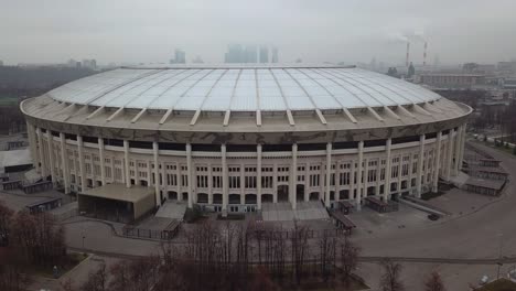 Orbit-drone-shot-of-the-Luzhniki-Stadium-in-Moscow,-Russia,-showing-the-industrial-city-in-the-background