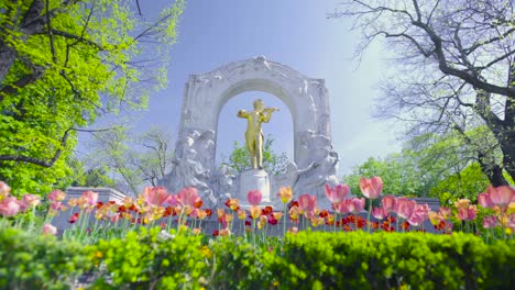 Toma-Deslizante-De-La-Estatua-De-Johann-Strauss-Con-Una-Hermosa-Pradera-De-Flores-En-Frente