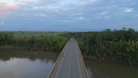 Aerial-View-of-Cauca-River-Flying-Over-Bridge-with-Passing-Motorcycles-at-Sunset