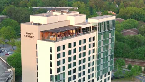 Drone-shot-of-Tourists-sitting-at-Hyatt-Centric-4-star-hotel-rooftop-restaurant-and-bar-in-Buckhead-surrounded-by-green-trees-landscape