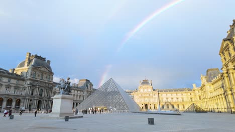 Colorido-Arco-Iris-Sobre-La-Pirámide-De-Cristal-Del-Louvre-Y-El-Palacio-Mientras-Los-Visitantes-Hacen-Cola-Para-Visitar-El-Museo-En-París,-Francia