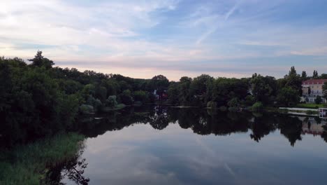 Tennis-stadium-with-red-clay-courts,-surrounded-by-a-lush-green-forest-and-a-small-lake