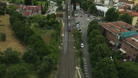 Train-tracks-passing-through-a-suburban-area-with-trees-and-houses,-aerial-view