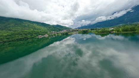 Ruhige-Luftaufnahme-Des-Lago-Di-Levico-Mit-üppigen-Grünen-Hügeln-Und-Stadtreflexionen-An-Einem-Bewölkten-Tag