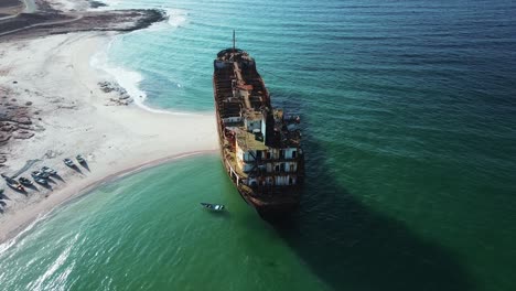 Aerial-view-of-a-shipwreck-on-the-rugged-coast-of-Socotra-Island,-with-turquoise-waters-contrasting-against-the-rusting-vessel-and-rocky-shoreline