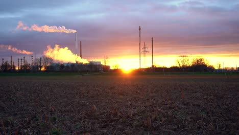 Sonnenaufgang-Hinter-Einer-Chemiefabrik-Mit-Von-Hinten-Beleuchteten-Rauchemissionen,-Die-Aus-Schornsteinen-Aufsteigen