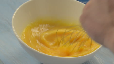 Beating-eggs-in-a-white-bowl-on-a-blue-wooden-background