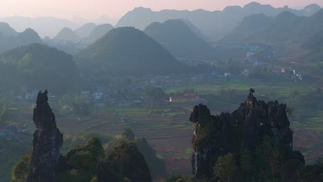 This-drone-footage-captures-a-misty-morning-in-Ha-Giang,-Vietnam,-highlighting-the-serene-beauty-of-a-small-town-nestled-among-terraced-rice-fields-and-surrounded-by-lush-green-mountains