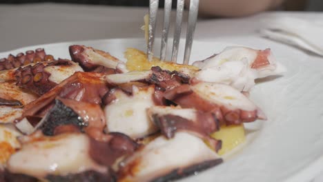 A-woman-picking-some-cooked-octopus-garnished-with-olive-oil-and-paprika-from-her-plate-at-one-of-the-finest-restaurant-in-Madrid,-Spain