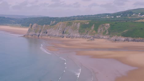 Strand-Von-Three-Cliffs-Bay-An-Einem-Heißen-Sommertag-Mit-Sanft-Hereinrollenden-Wellen-Und-Felsiger-Küste-In-Swansea,-Gower,-Großbritannien,-4k