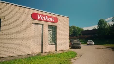 A-brick-stone-shop-labeled-Veikals-in-a-Baltic-village-in-Latvia,-with-two-parked-cars-visible-in-the-frame