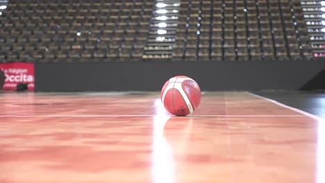 Tiro-Lento-Y-Revelador-De-Una-Pelota-De-Baloncesto-Tirada-En-La-Cancha-Dentro-De-Un-Estadio-Vacío