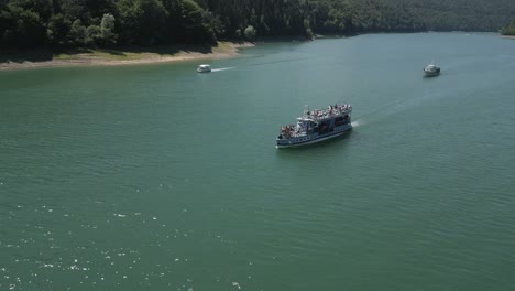 orbiting-aerial-of-boats-loaded-with-tourists-enjoying-the-warm-summer-sun-on-Lake-Bicaz,-Romanian-summer-tourism-hotspot