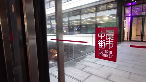 Rotes-Central-Market-Schild-An-Der-Glastür-In-Hongkong-Mit-Menschen-Im-Hintergrund