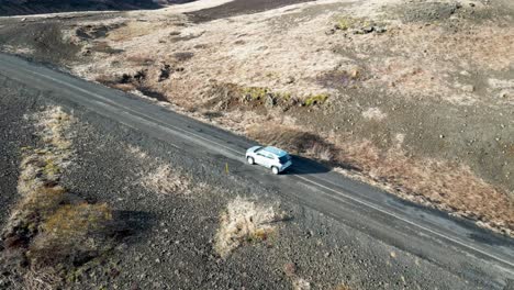 Driving-in-Iceland,-an-SUV-navigates-a-gravel-road-through-mountains-and-moss-covered-landscapes