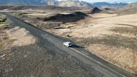 Driving-in-Iceland,-an-SUV-navigates-a-gravel-road-through-mountains-and-moss-covered-landscapes,-A-bird's-eye-view-shows-the-vehicle-amidst-Iceland's-wild-beauty