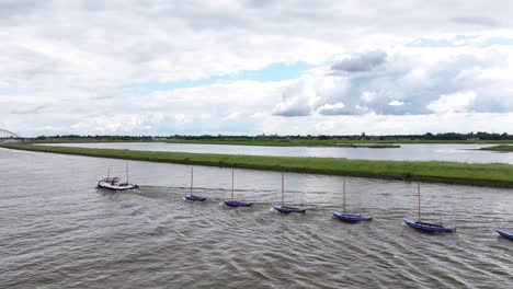 Una-Lancha-Remolcando-Una-Serie-De-Siete-Pequeñas-Embarcaciones-En-El-Río-Noord-En-Hendrik-ido-ambacht,-Holanda-Del-Sur,-Países-Bajos---Toma-Aérea-De-Drones