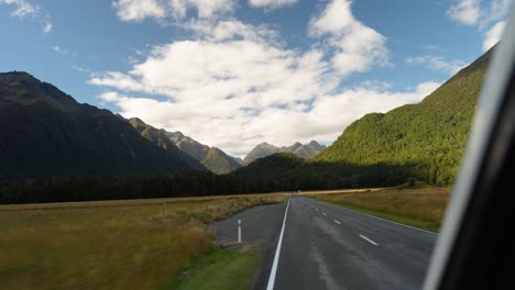 Scenic-road-in-New-Zealand-leading-towards-a-mountain-range,-with-a-clear-sky-and-lush-green-landscape