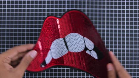 Red-bitten-lips-sequin-patch-being-positioned-on-a-grid-surface-by-hands