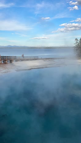 Vertical-4k,-Woman-With-Backpack-Walking-on-Trail-Between-Hot-Spring-Pool-and-Lake-in-Yellowstone-National-Park,-Wyoming-USA