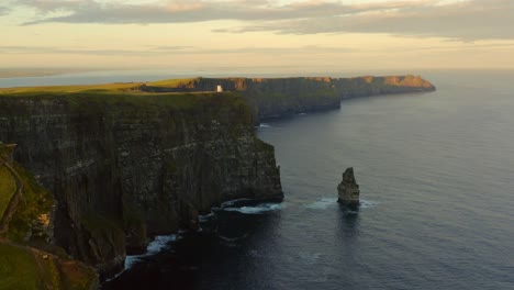 Aerial-descent-captures-the-breathtaking-sunrise-at-the-Cliffs-of-Moher,-illuminating-the-rugged-landscape-in-warm-hues