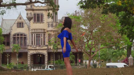 A-girl-in-a-blue-dress-explores-a-sunny-park,-castles-visible-in-the-background