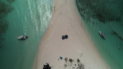 A-tropical-sandbar-surrounded-by-turquoise-waters-with-boats-docked-nearby,-aerial-view