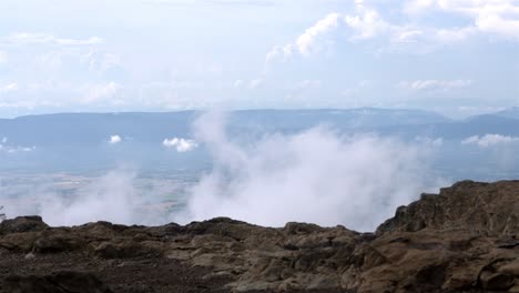 Imágenes-Tomadas-En-Cámara-En-Mano-Desde-La-Cima-De-Una-Montaña-Rocosa-Capturan-Una-Vista-Impresionante-De-Las-Nubes-Moviéndose-Sobre-Tierras-De-Cultivo-Distantes